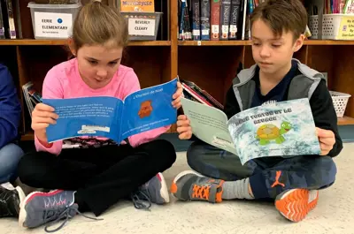 two students sitting on floor reading books